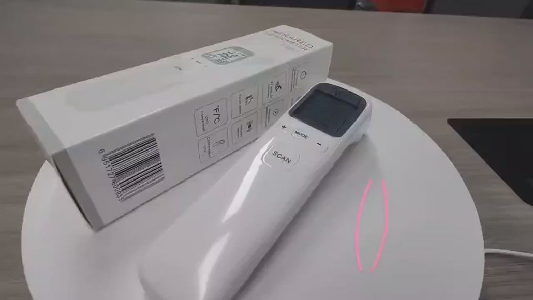 A MediWares digital infrared thermometer resting on its box which has instructional icons on the side, placed on a plain surface. Pink markings highlight an area on the box.